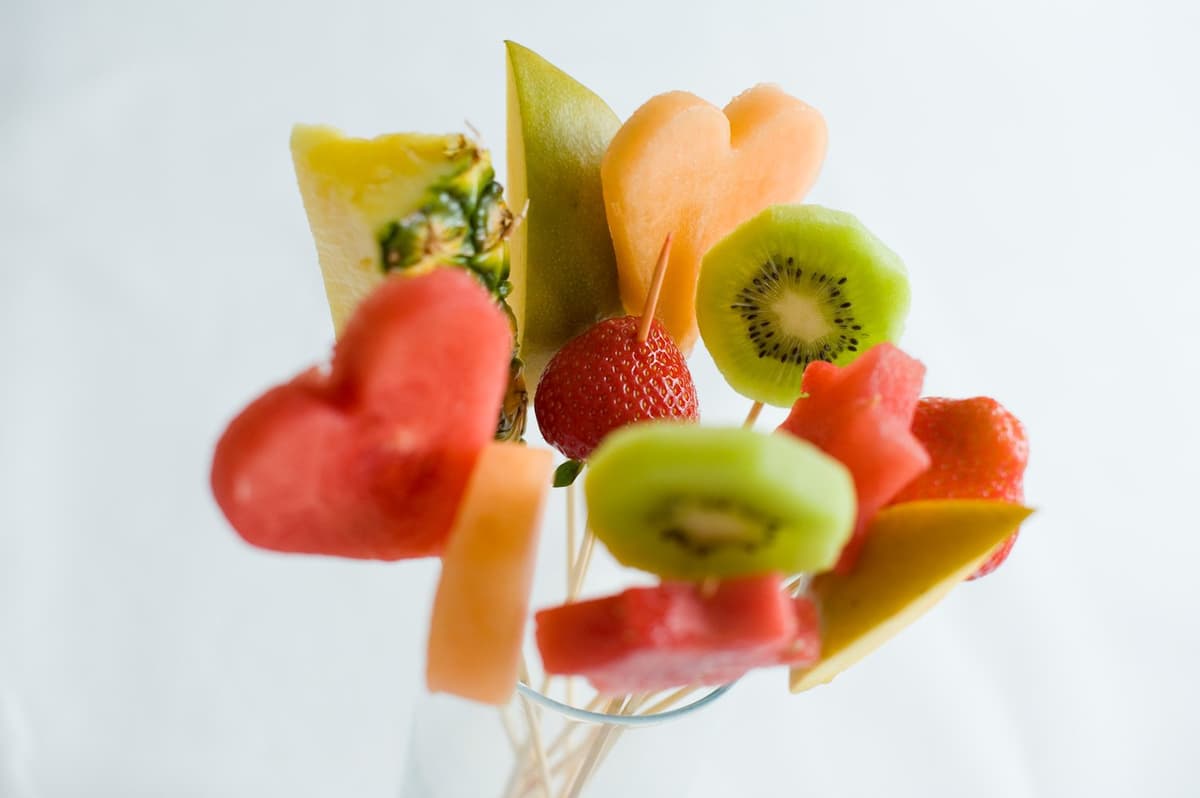 Färgglada fruktspett med hjärtformade bitar av melon, kiwi, jordgubbar och ananas, arrangerade i ett glas.