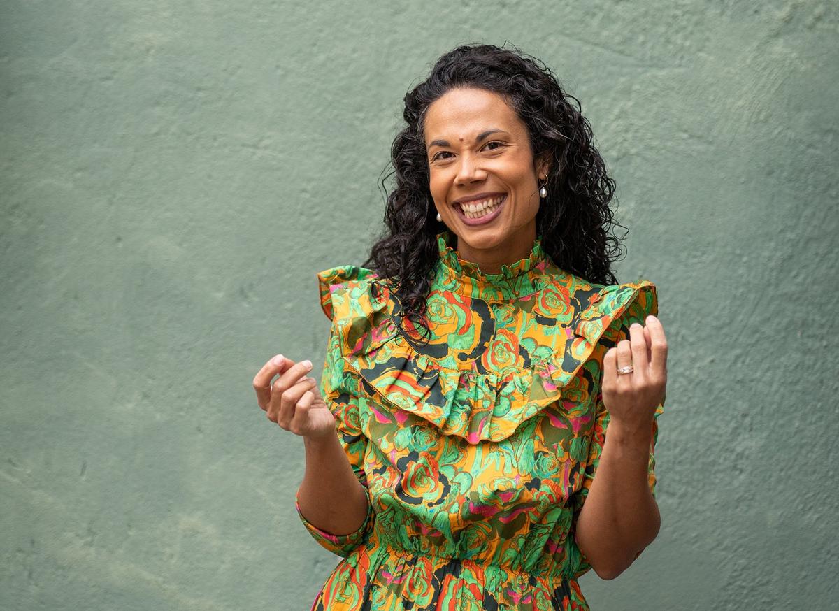 En mörkhårig kvinna i färgglad klänning ler glatt mot kameran.