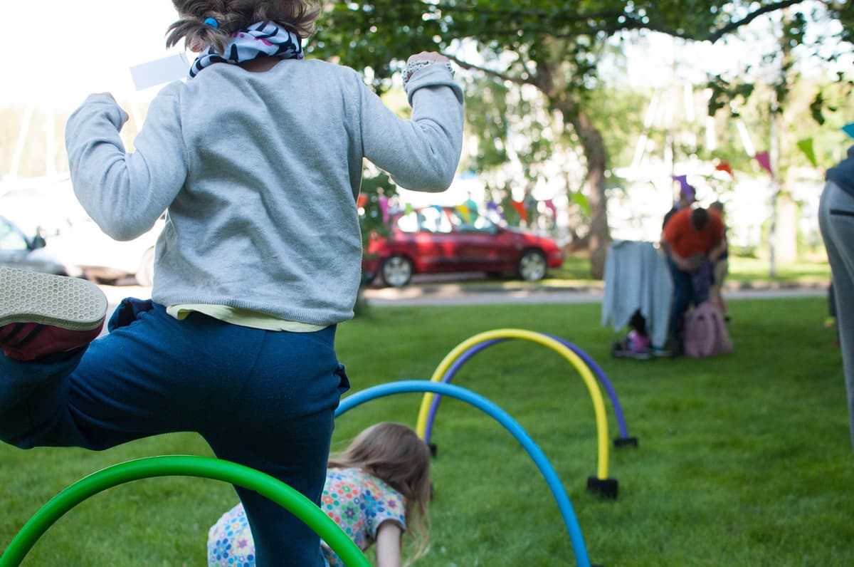 Ett barn hoppar över färgglada hinder utomhus. Bilden är tagen bakifrån, så barnet går ej att känna igen.