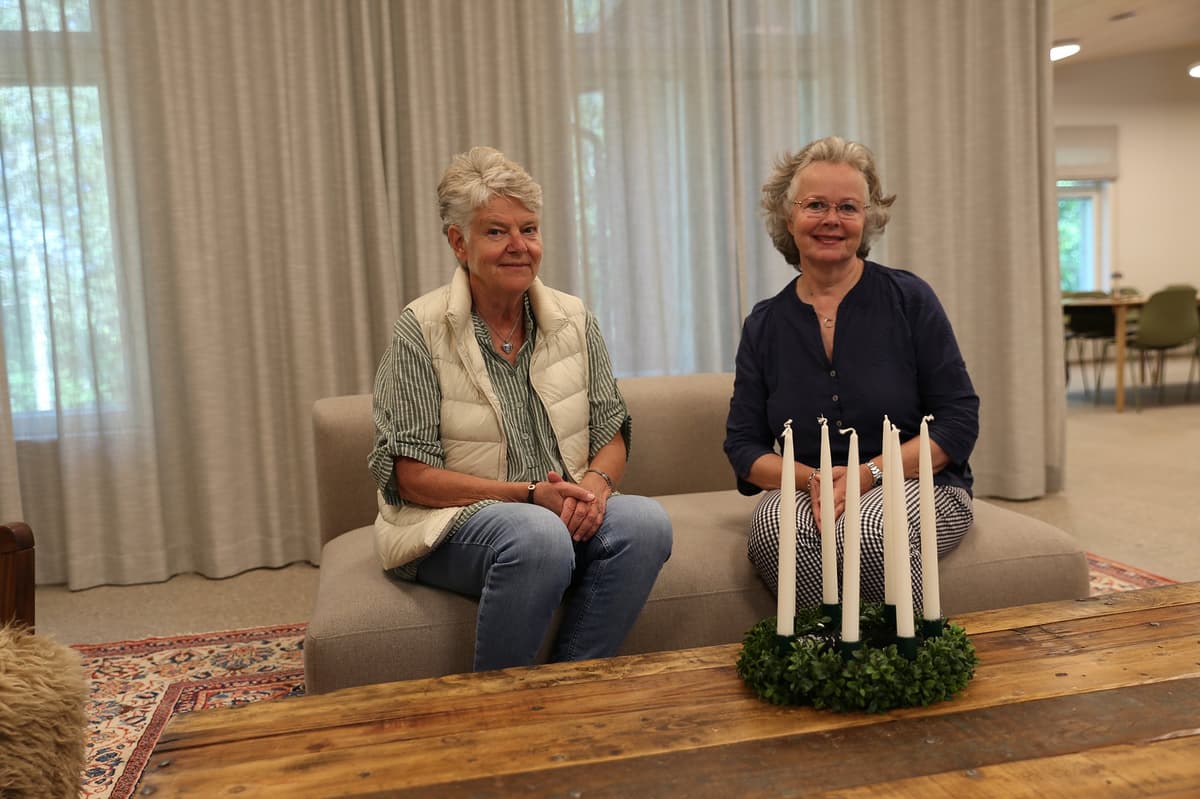 Två pensionerade damer sitter på en soffa och ser glada ut. På bordet framför dem finns en luciakrona, med släckta ljus. 