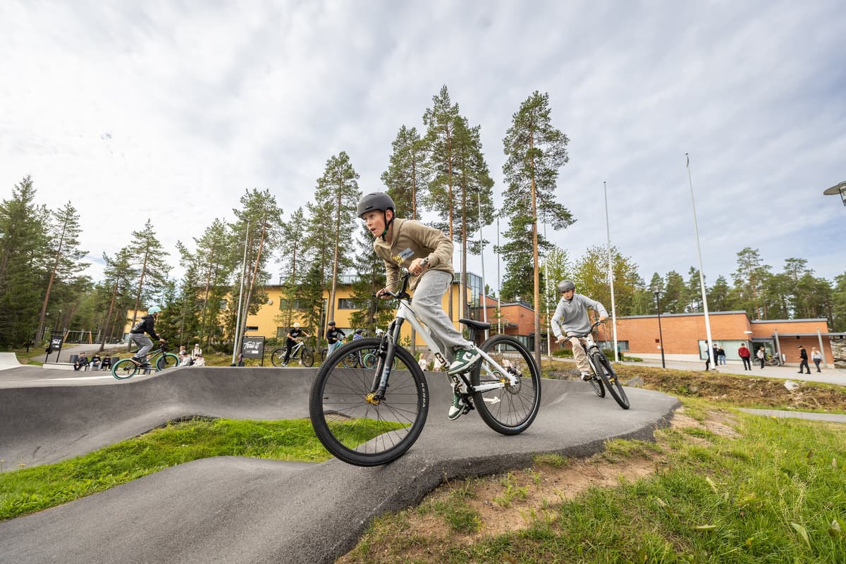 Högstadieelever cyklar på en vågformad bana, pumptrack, utanför sin skola.