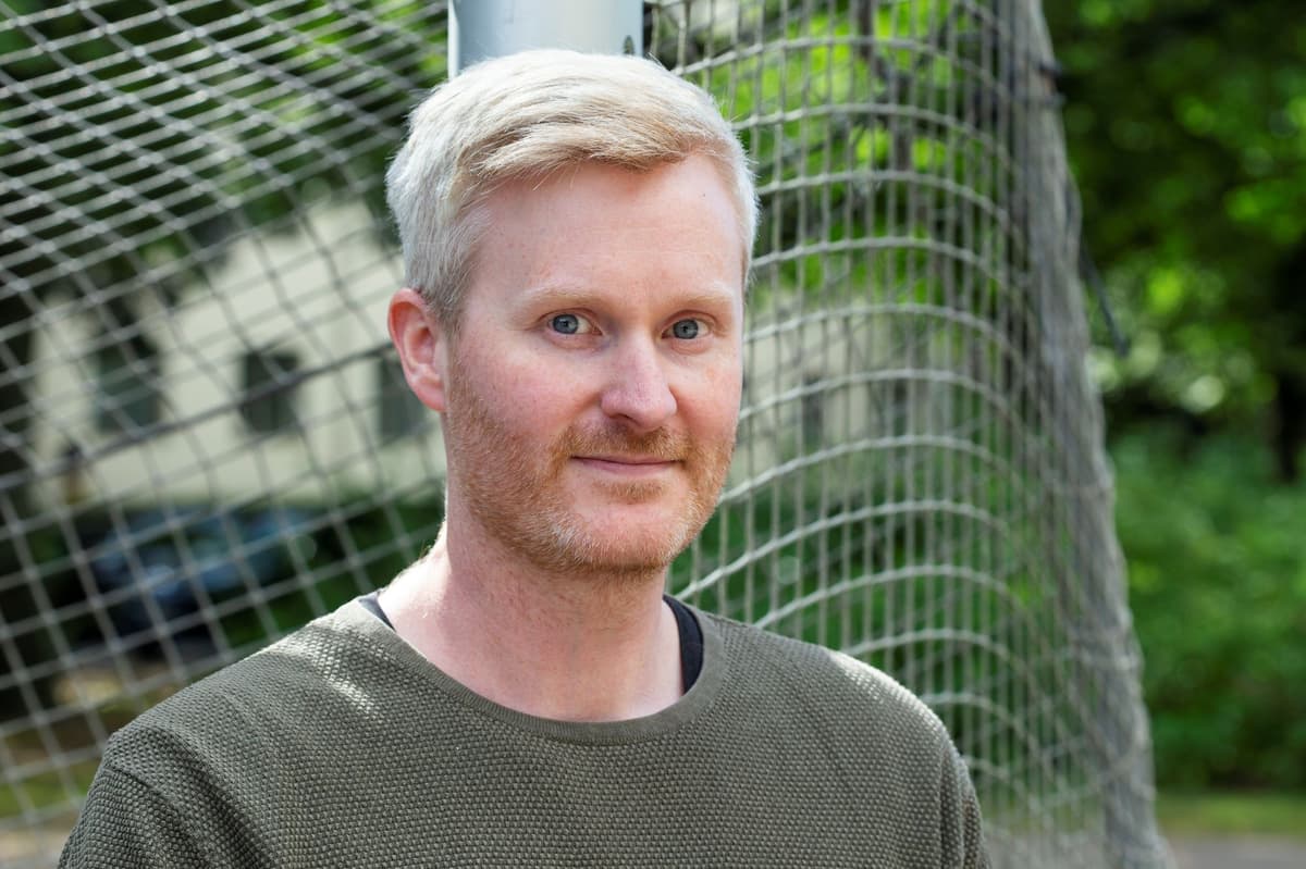Man framför ett fotbollsmål som tittar rakt in i kameran.
