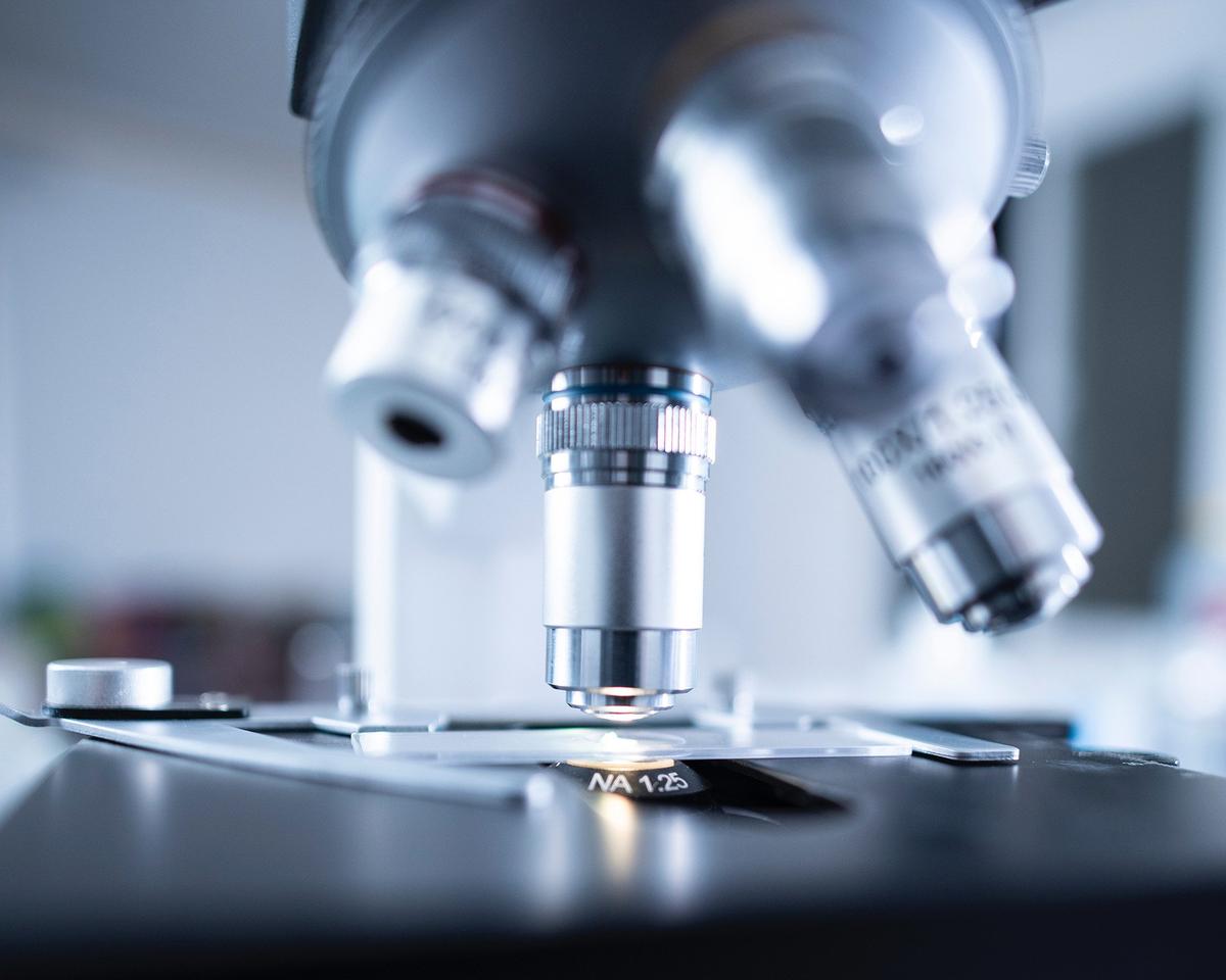 Close-up of a microscope’s objective lenses positioned above a glass slide on the stage. The image has a cool, clinical tone with a shallow depth of field, suggesting a laboratory or research setting.
