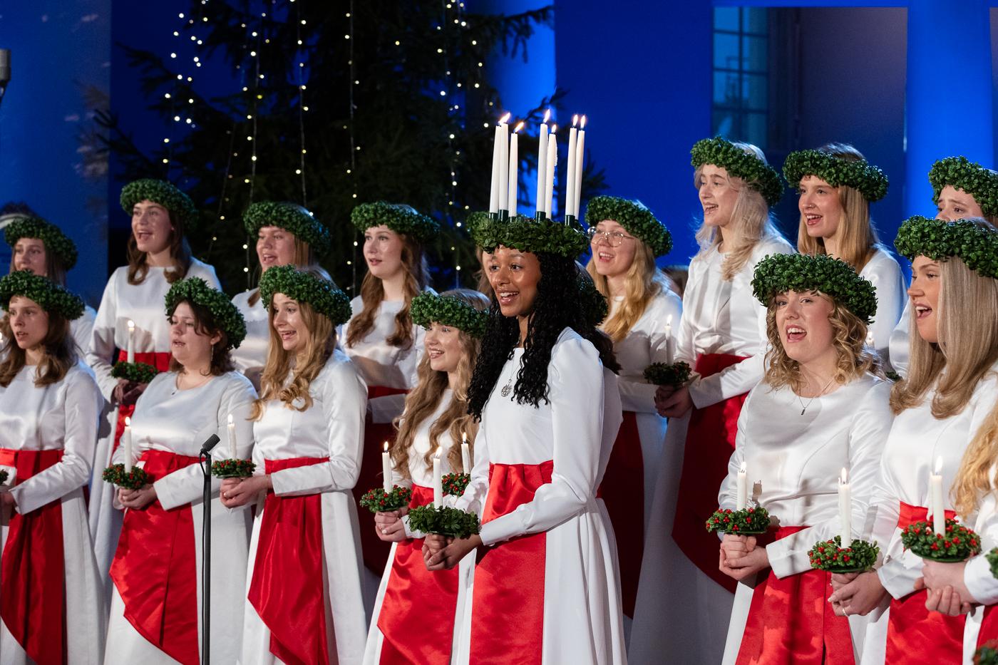 Lucia med följe står upp under ett uppträdande och sjunger. 