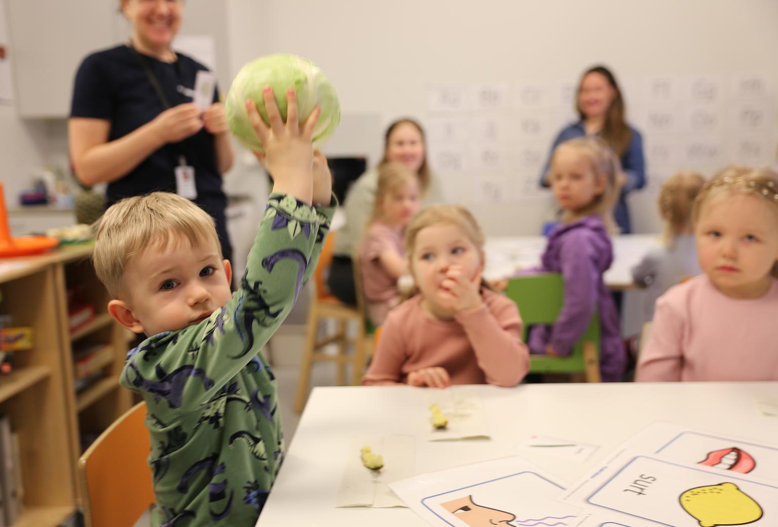 En liten pojke lyfter upp ett kålhuvud med sina båda händer och ser in i kameran.