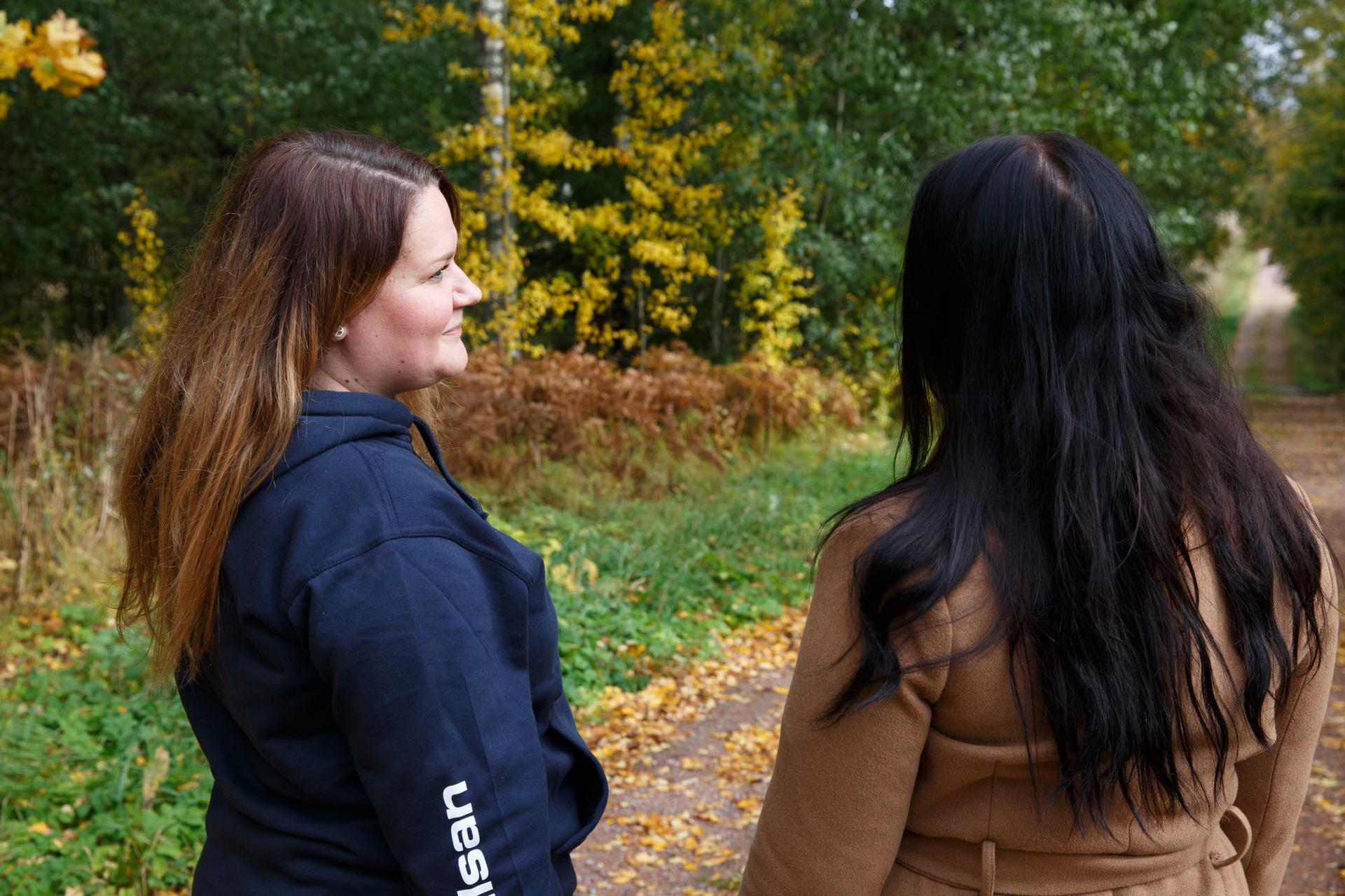 Två personer promenerar och samtalar längs en skogsstig en höstdag.