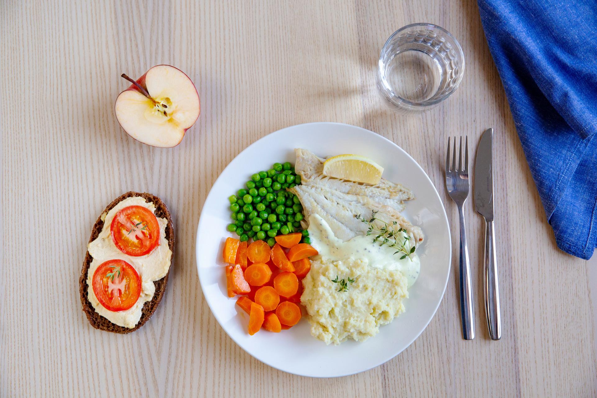 Tallrik med fisk, mos och grönsaker. Smörgås, vattenglas och bestick bredvid.