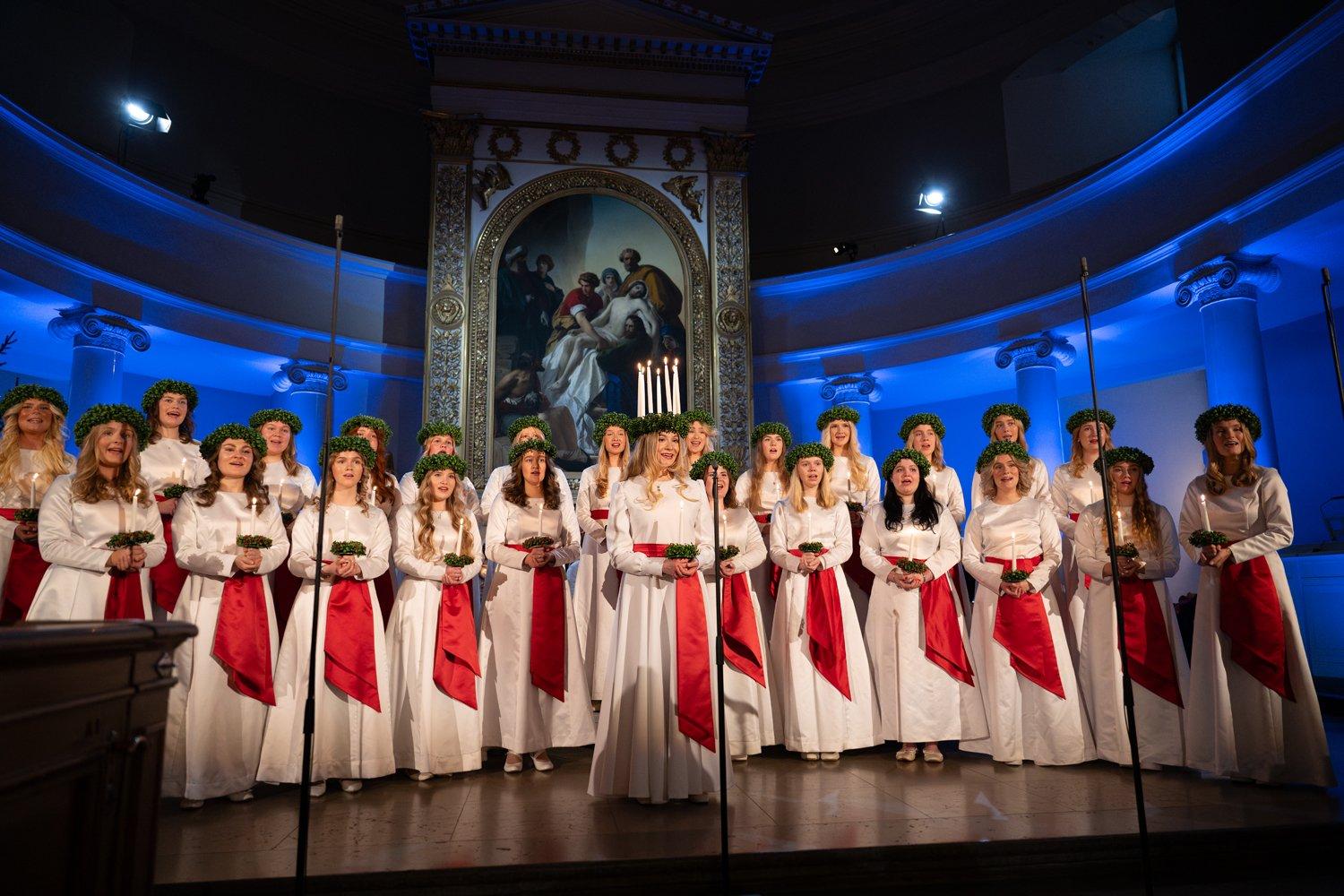 Barnkören, Luciakören och Finlands Lucia ställer upp för körsång i en domkyrka upplyst i festliga blåaktiga färger.