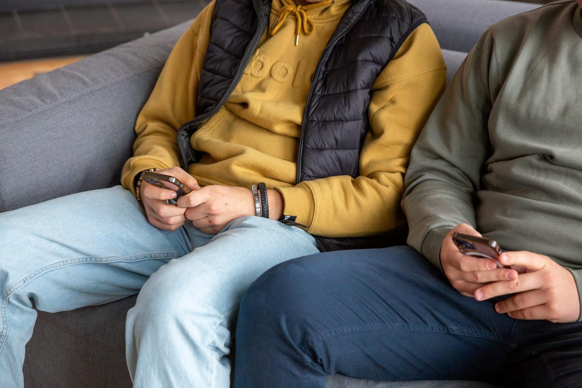Två pojkar sitter i en soffa och läser på sina mobiltelefoner.