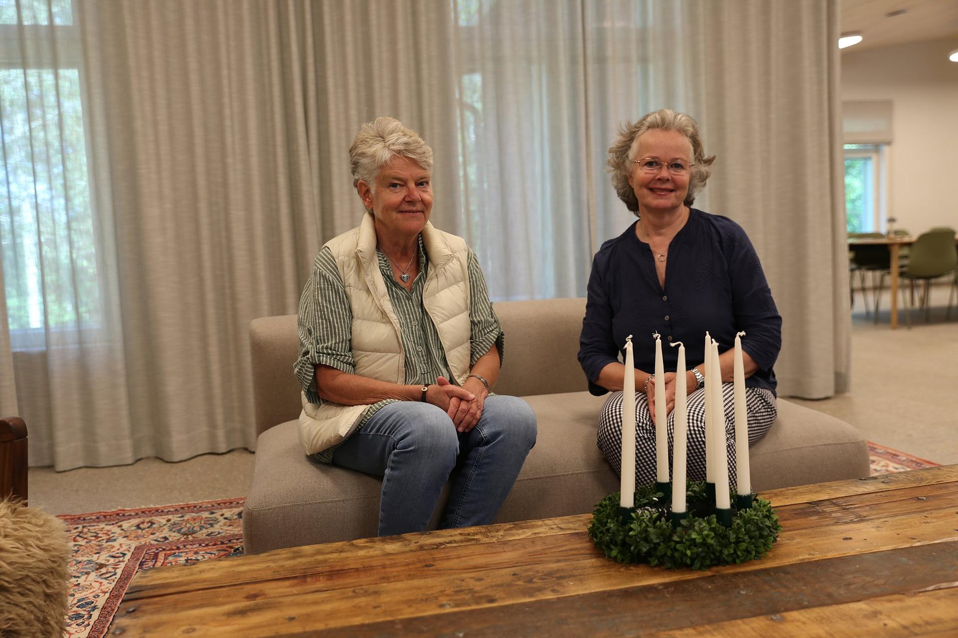 Två pensionerade damer sitter på en soffa och ser glada ut. På bordet framför dem finns en luciakrona, med släckta ljus.