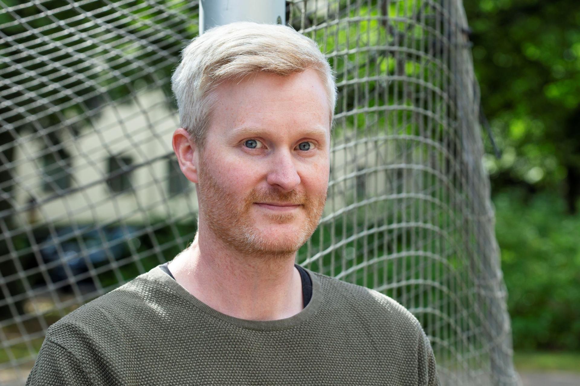 Man framför ett fotbollsmål som tittar rakt in i kameran.