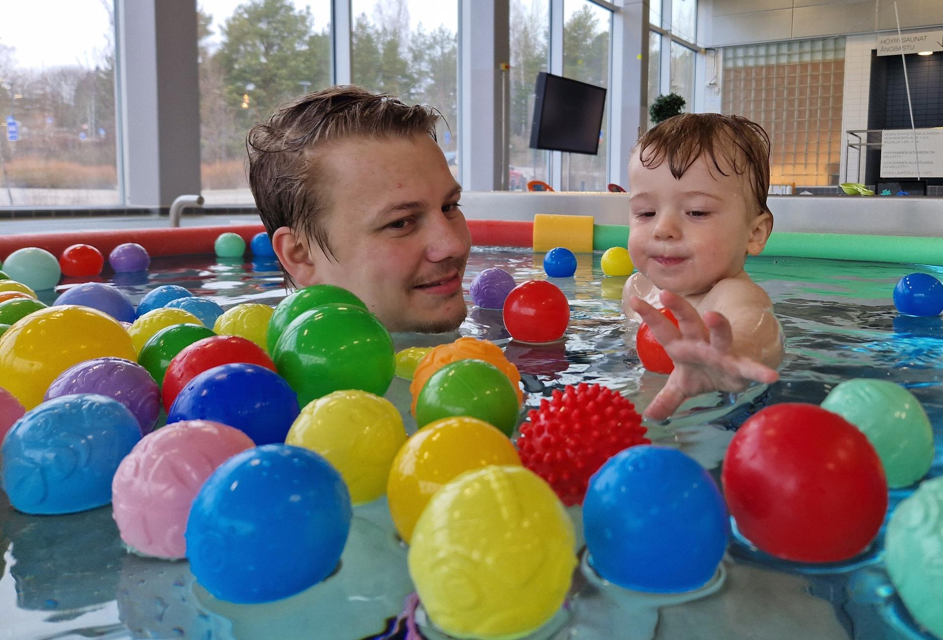 Ett barn simmar i en simhall med sin pappa bland en massa färggranna små plastbollar. 