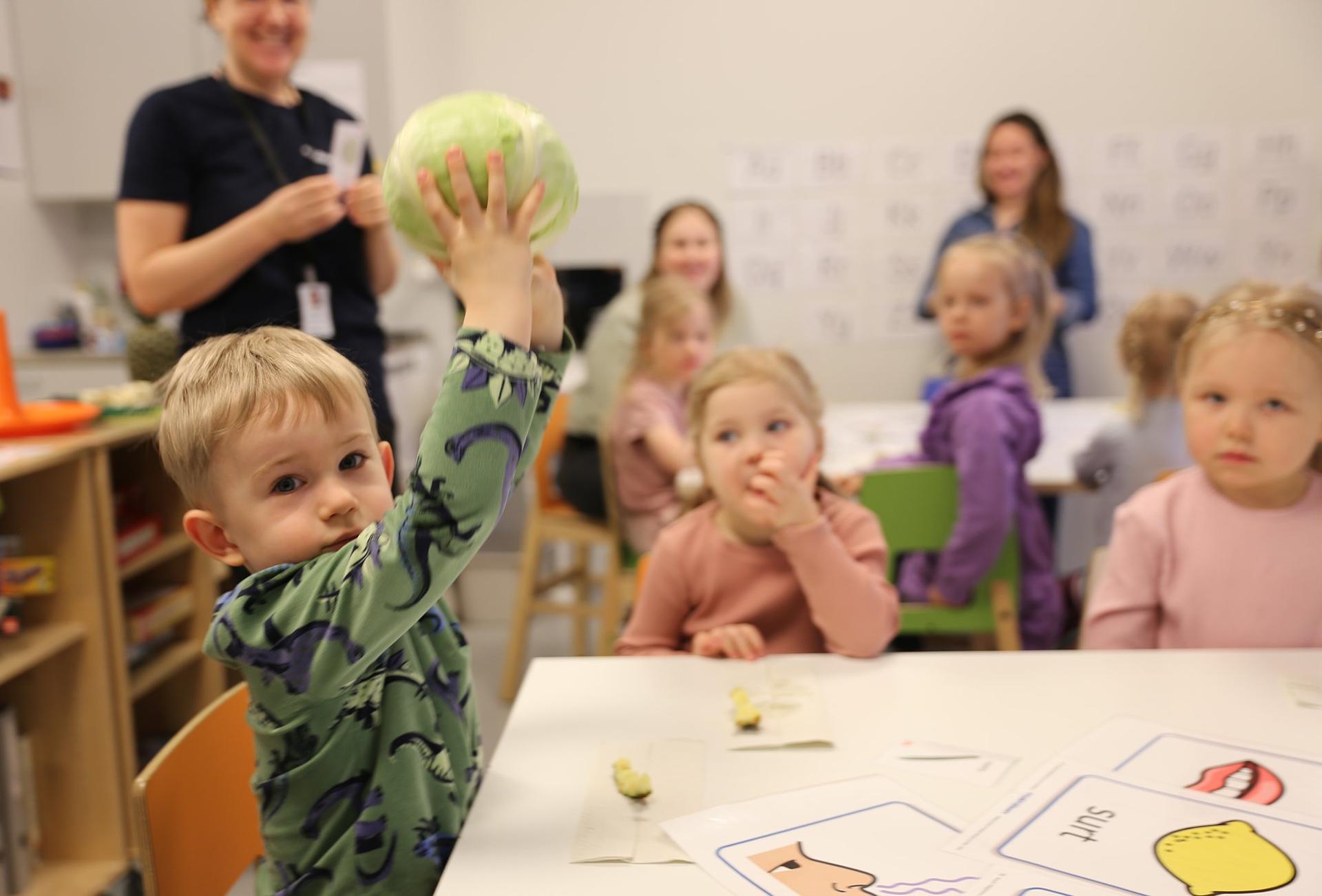 En liten pojke lyfter upp ett kålhuvud med sina båda händer och ser in i kameran.