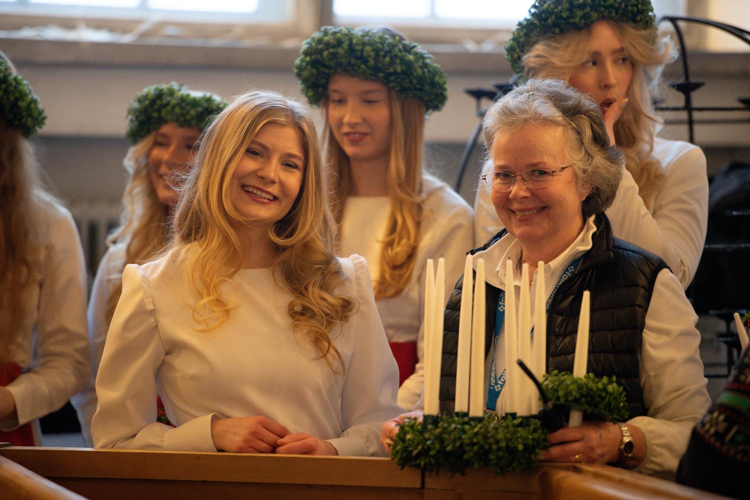 En ung kvinna sitter brevid en äldre kvinna, som håller i en luciakrona.