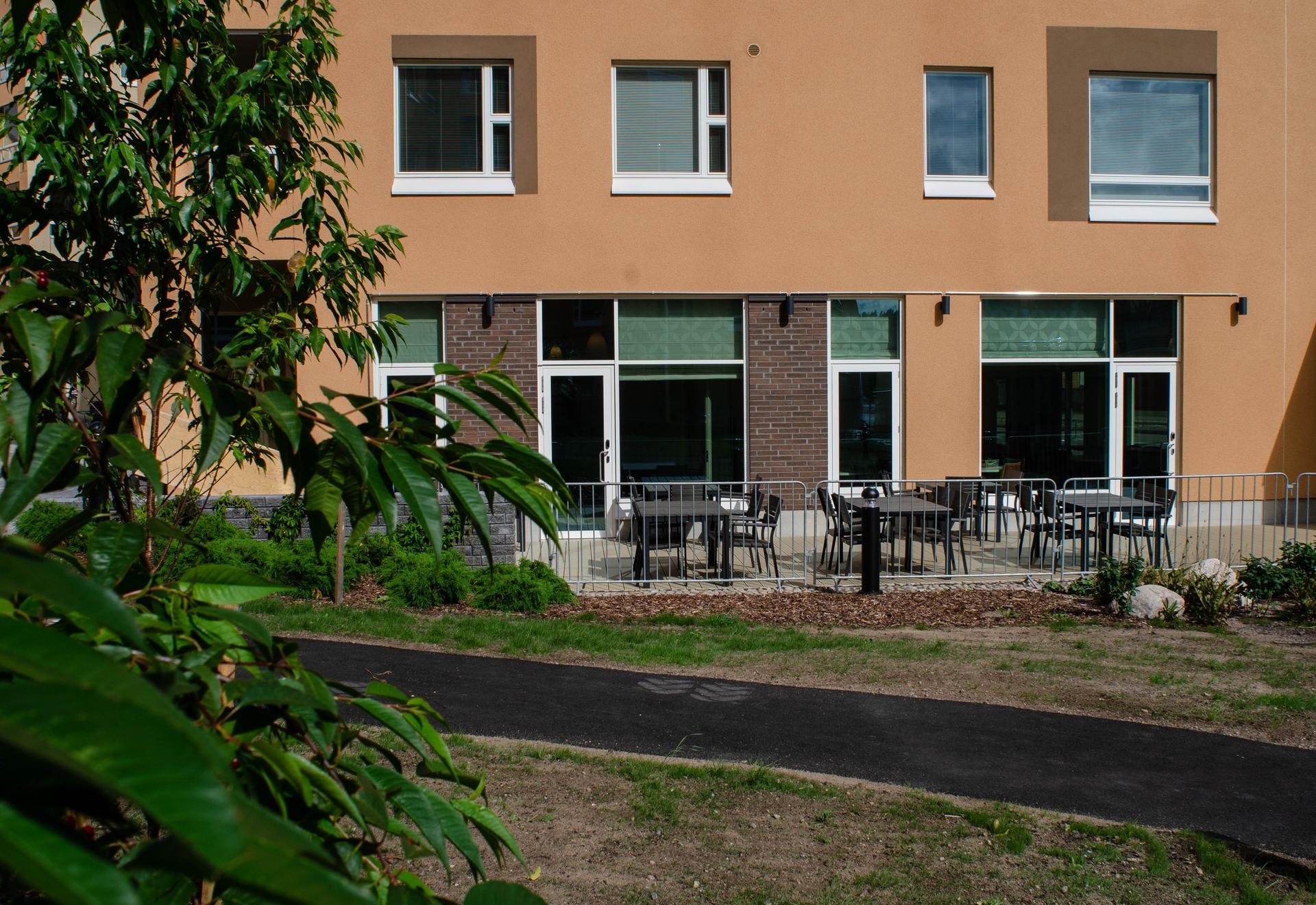 Uteplats med bord och stolar utanför Folkhälsans hus. Terrassen är avgränsad med räcken och omges av planteringar och gångstig.