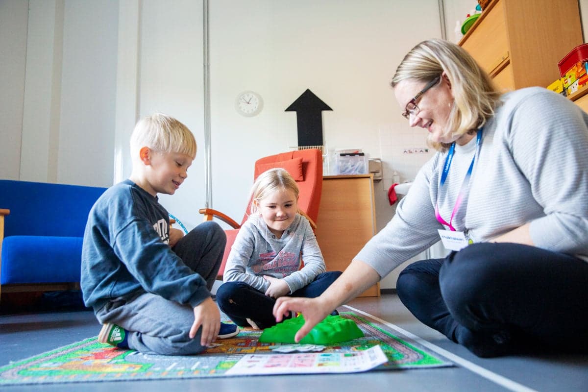 Barn sitter på golvet och spelar ett spel tillsammans med en vuxen i en trygg inomhusmiljö.