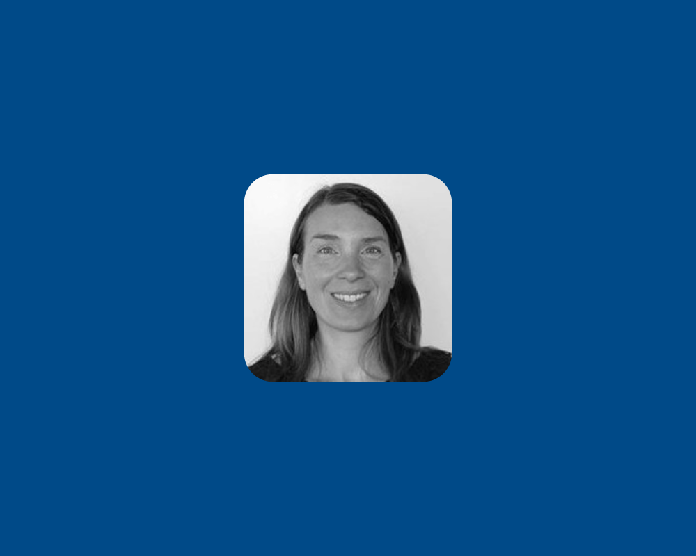 A smiling woman with shoulder-length dark hair is shown in a black-and-white headshot, facing the camera. The portrait is cropped closely around her face against a plain background.