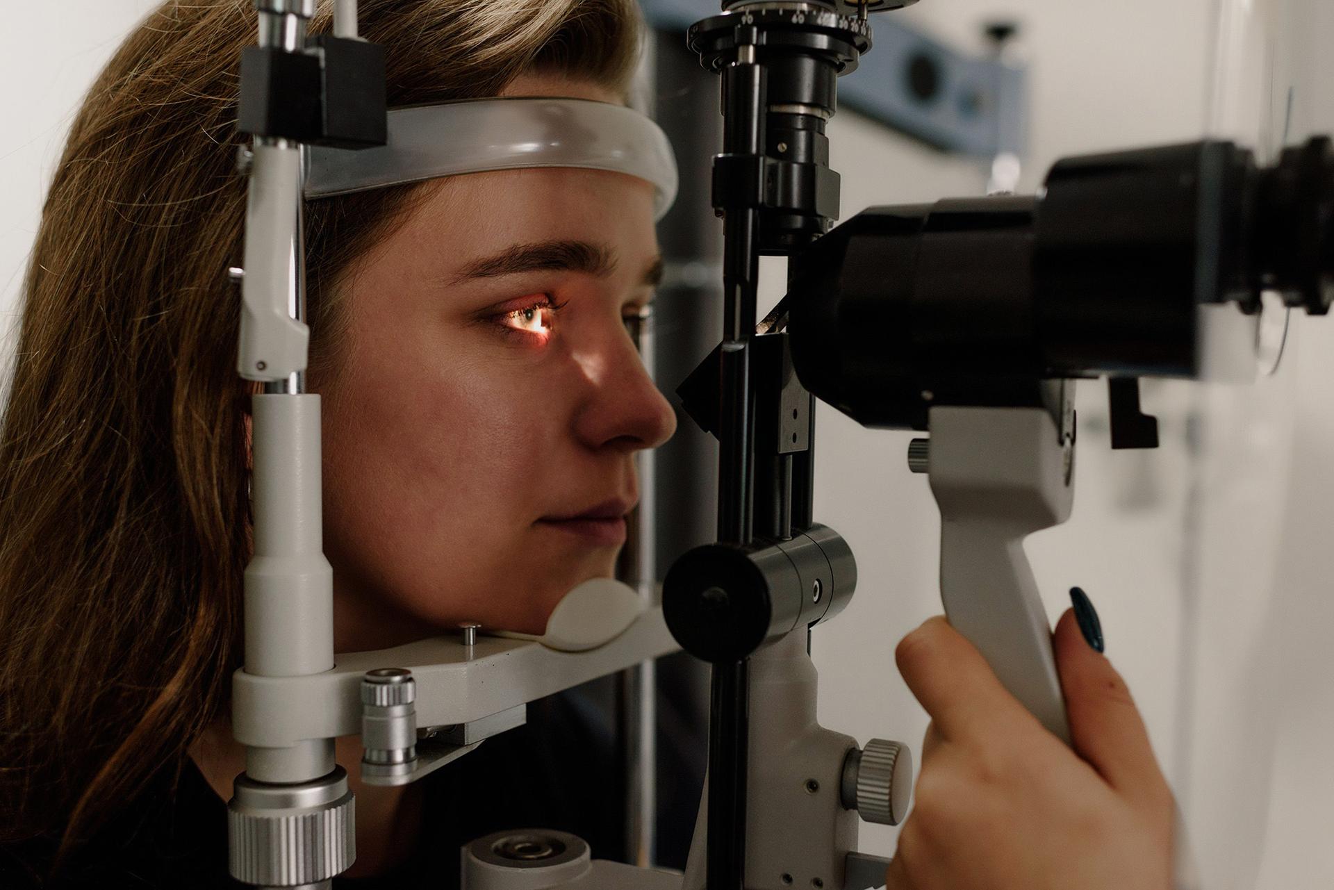 A person is having their eye examined during an eye checkup. A bright light is directed at the eye while the person rests their chin and forehead against the examination device.