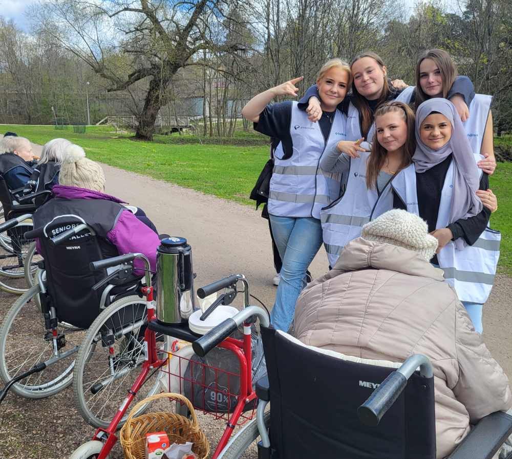 Glada studerande fr&aring;n Prakticum och n&aring;gra &auml;ldre h&aring;ller en kaffepaus i en park n&auml;ra Haga hj&auml;ltegravar.