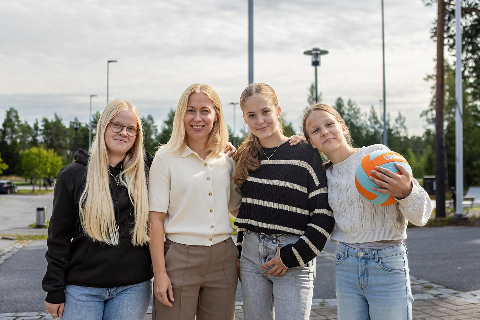 Tre kvinnliga elever och deras rektor står på en rad och håller i en volleyboll.