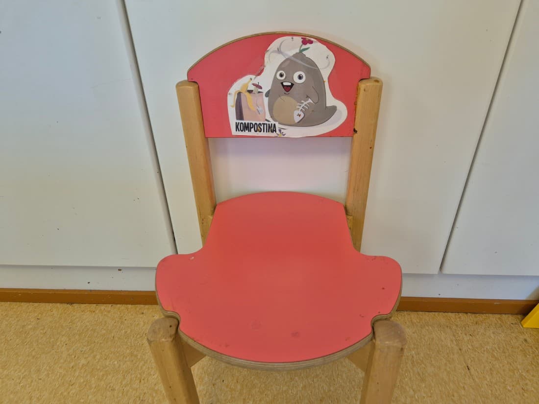En liten barnstol med en tecknad figur p&aring; ryggst&ouml;det d&auml;r det st&aring;r "Kompostina".