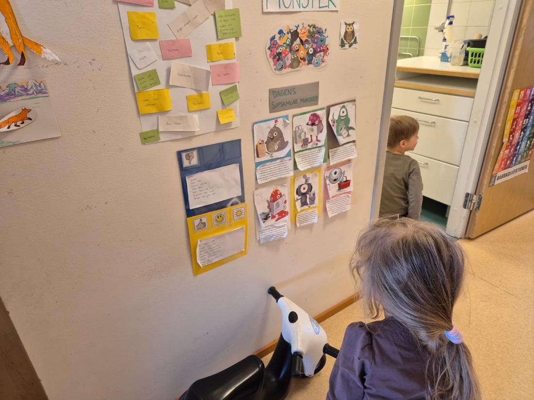 En liten flicka sitter p&aring; en trehjuling och tittar p&aring; en v&auml;g med teckningar av f&auml;rgranna "sopmonster".